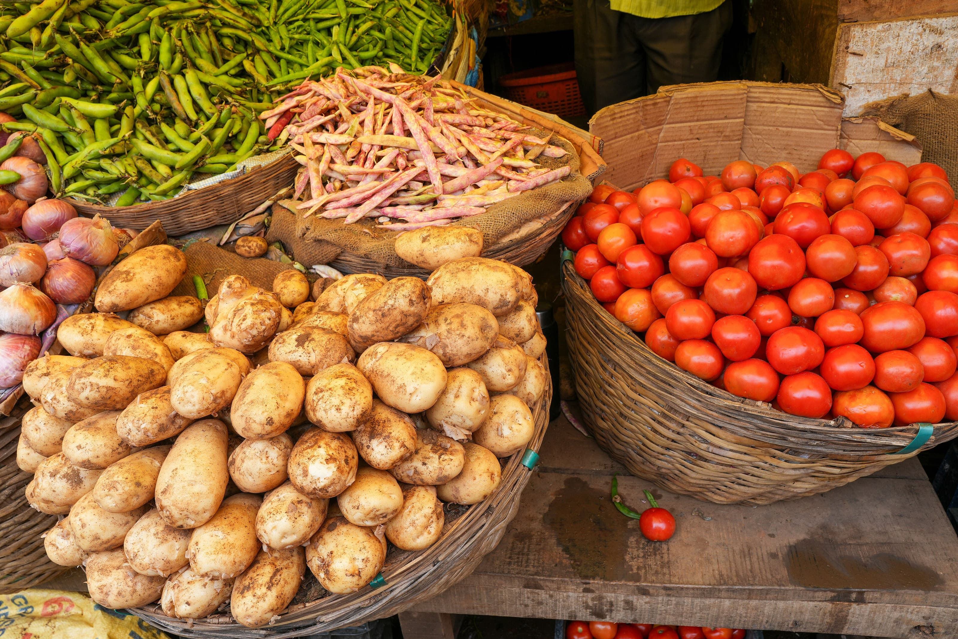 Baskets of potatoes, tomatoes, green chillies and beans on a market stall.