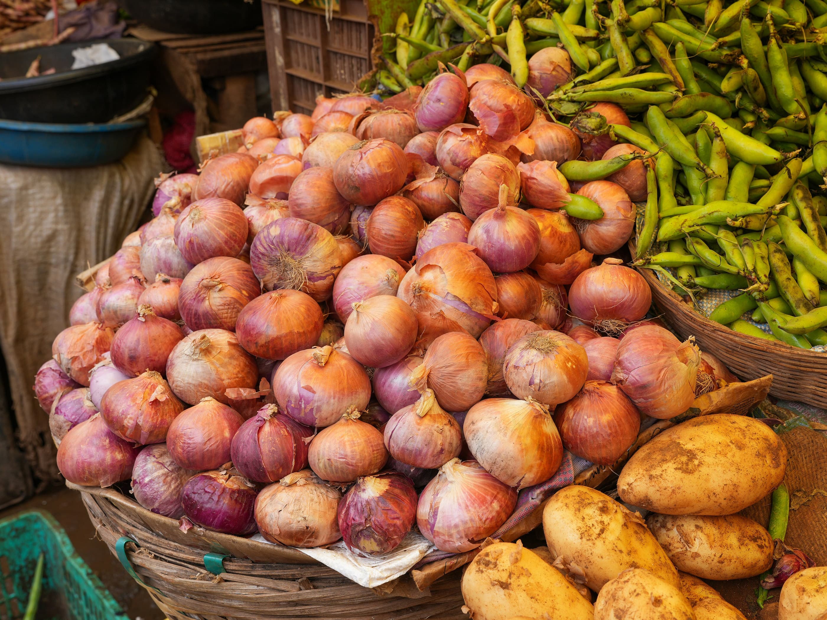 A heaped pile of red onions with potatoes and green chillies at a market stall.